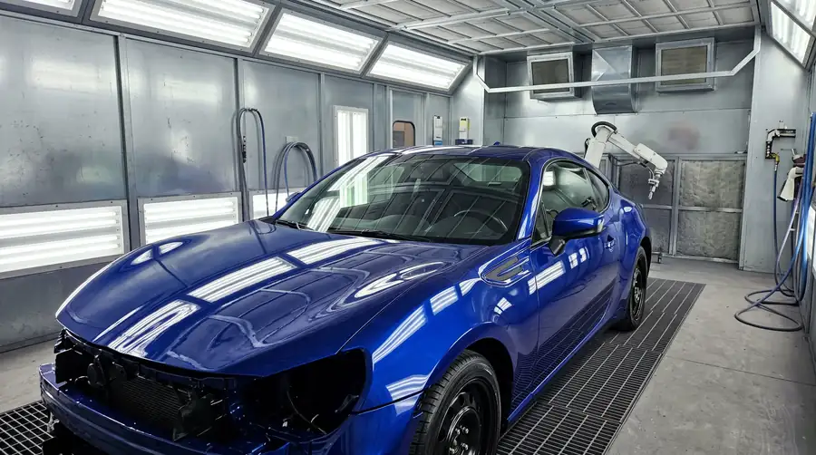 A freshly painted car body under booth lights with wet glossy clear coat