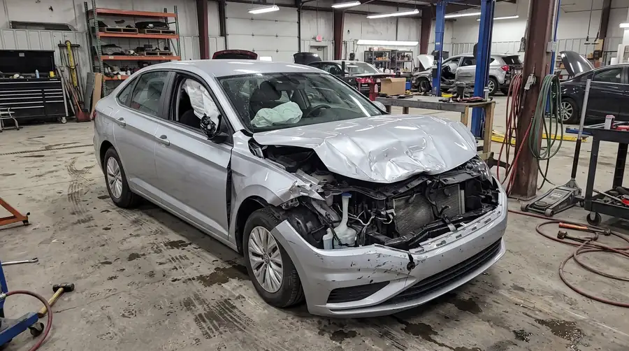 A severely damaged car with a crumpled front end in a body shop